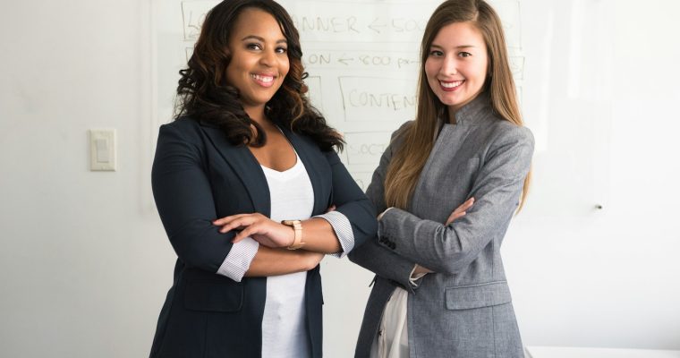 two women in suits standing beside wall